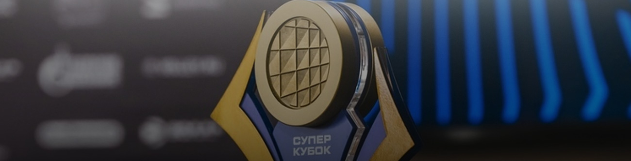 Трофей с надписью Супер Кубок на фоне темной сцены с размытыми логотипами. Трофей имеет золотистые и синие элементы с центральной круглой частью, украшенной узором