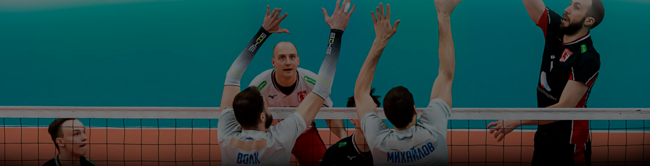 Спортивный момент: команда в белой форме блокирует удар соперника в черной форме во время волейбольного матча. Игроки сосредоточены и напряжены, мяч в центре внимания